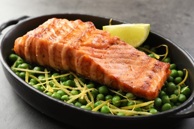 Photo of Delicious grilled salmon fillet with green peas and lime in baking dish on grey table, closeup