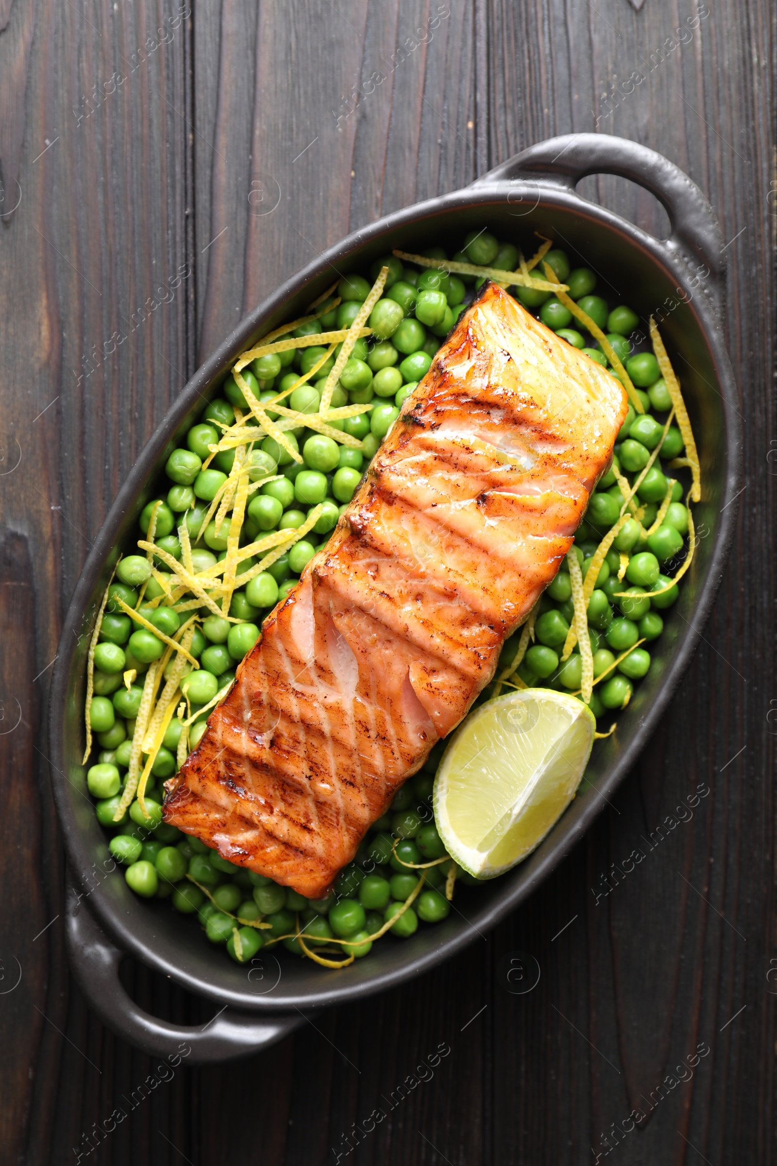 Photo of Delicious grilled salmon fillet with green peas and lime in baking dish on wooden table, top view