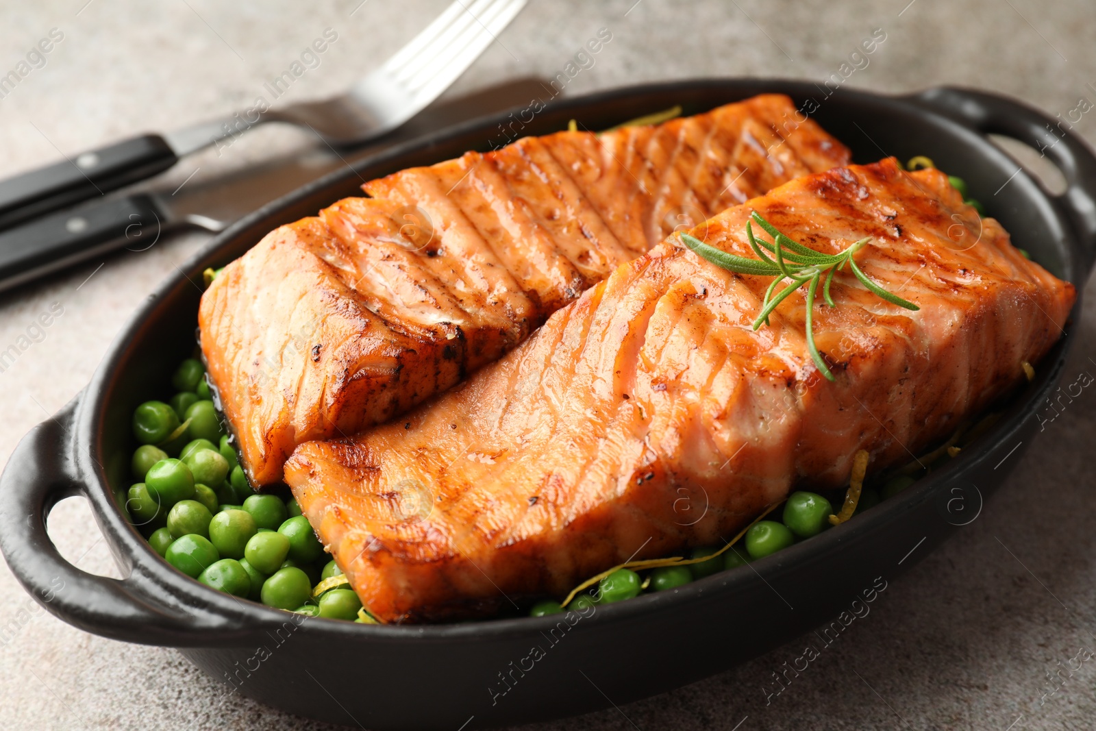 Photo of Delicious grilled salmon fillets with green peas in baking dish served on grey textured table, closeup