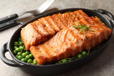 Delicious grilled salmon fillets with green peas in baking dish served on grey textured table, closeup