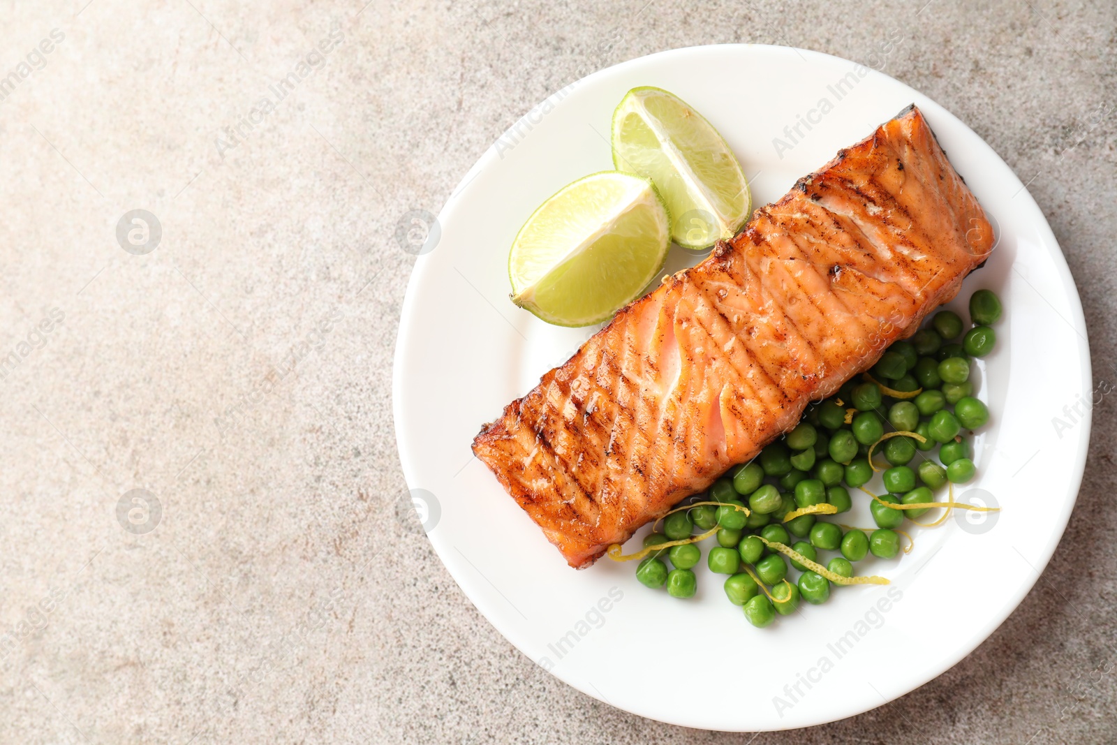 Photo of Delicious grilled salmon fillet with green peas and lime on grey textured table, top view. Space for text