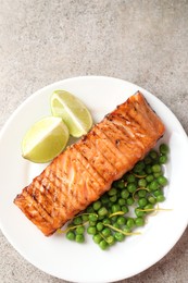 Photo of Delicious grilled salmon fillet with green peas and lime on grey textured table, top view