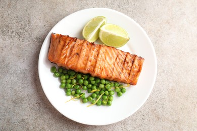 Delicious grilled salmon fillet with green peas and lime on grey textured table, top view