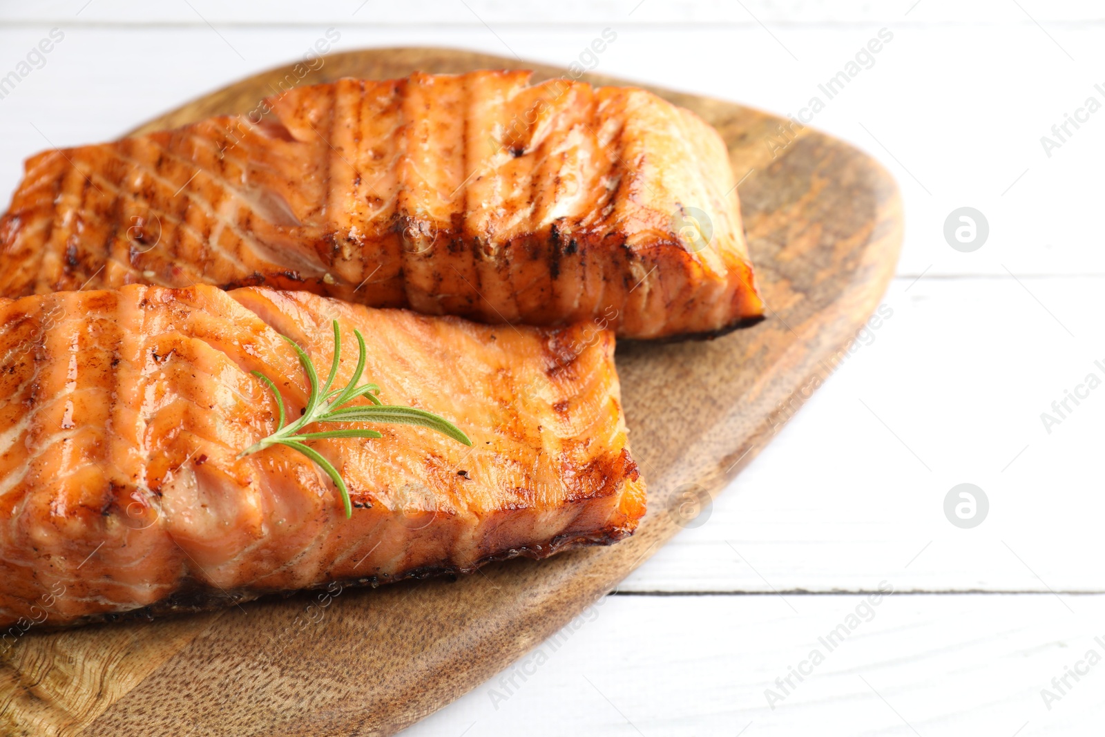 Photo of Delicious grilled salmon fillets with rosemary on white wooden table, closeup