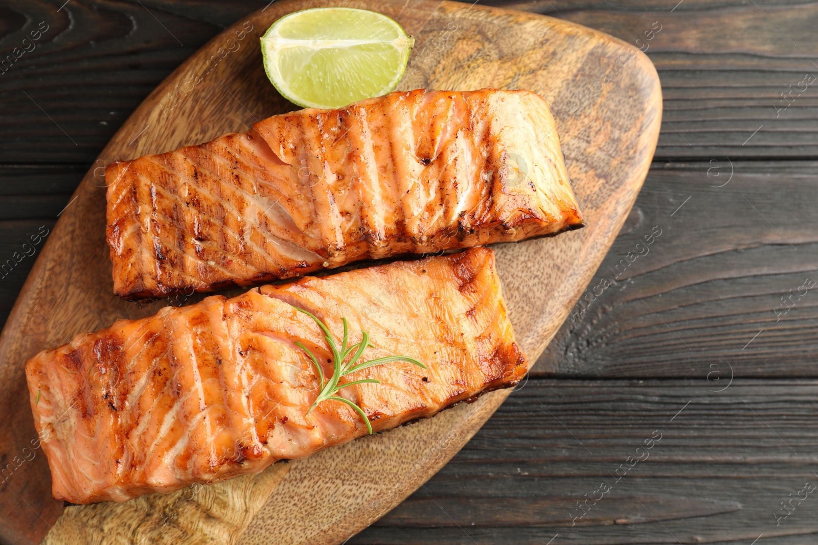 Photo of Delicious grilled salmon fillets with lime and rosemary on wooden table, top view