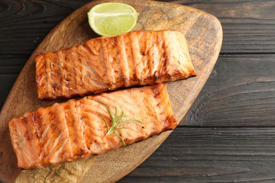 Photo of Delicious grilled salmon fillets with lime and rosemary on wooden table, top view