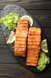 Photo of Delicious grilled salmon fillets with lettuce and lemon on wooden table, top view