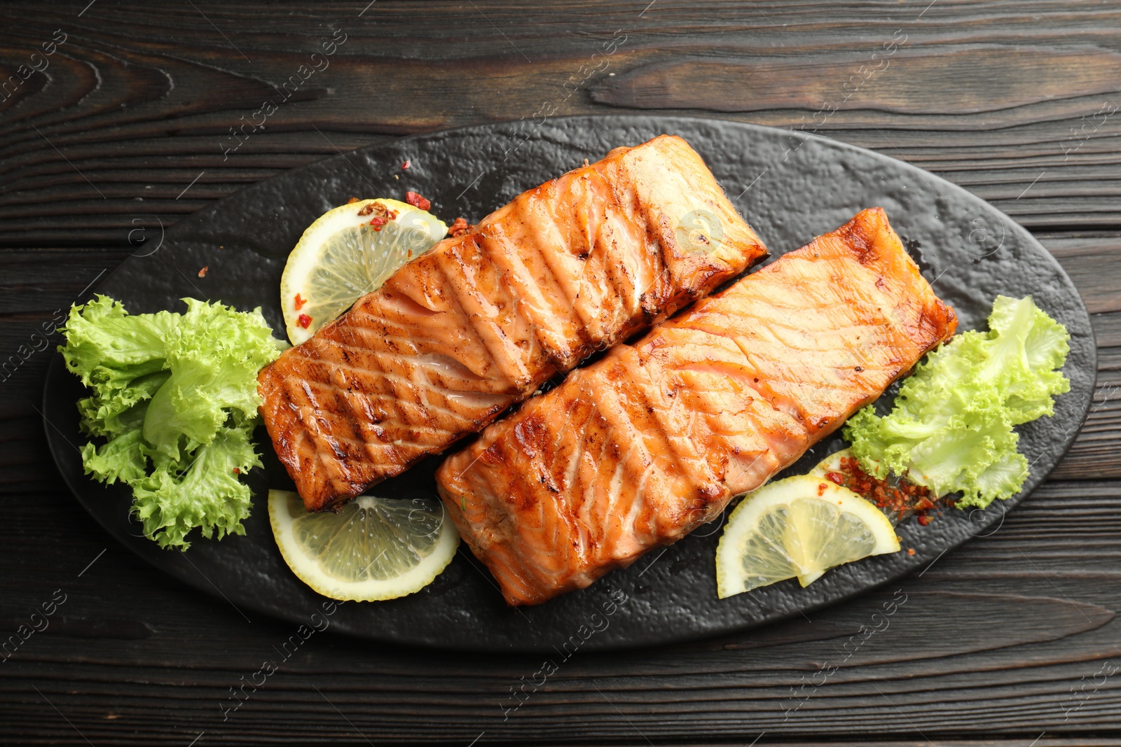 Photo of Delicious grilled salmon fillets with lettuce and lemon on wooden table, top view