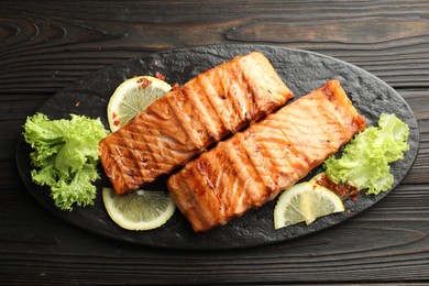 Delicious grilled salmon fillets with lettuce and lemon on wooden table, top view