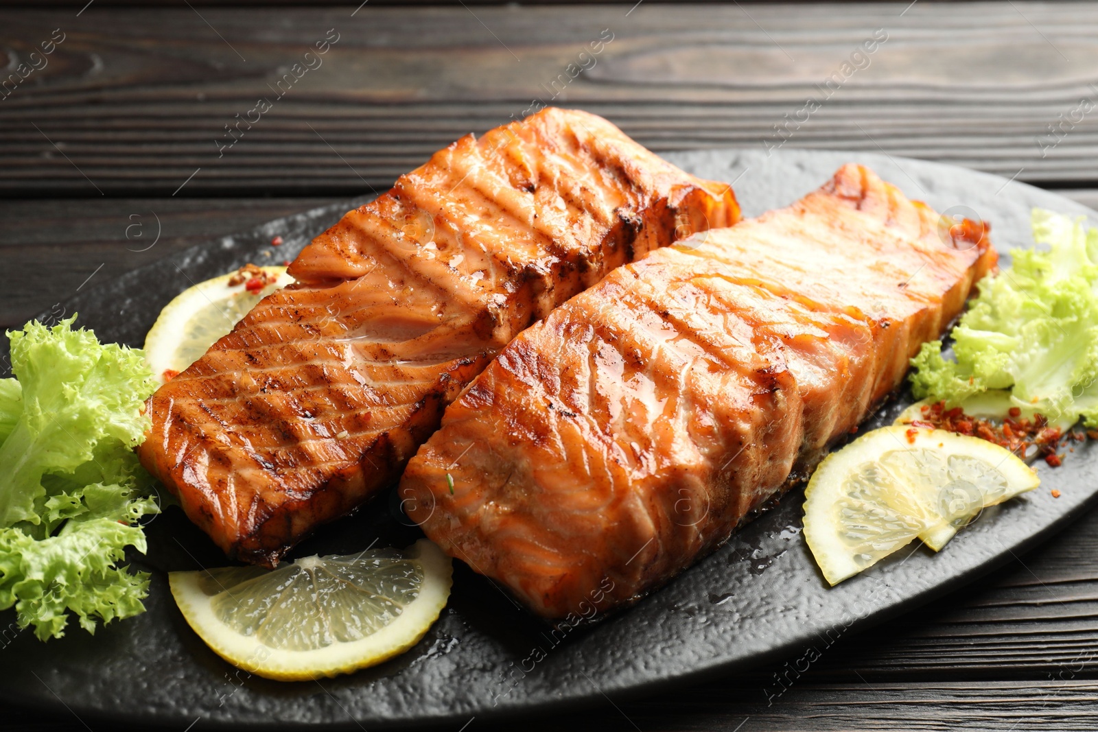 Photo of Delicious grilled salmon fillets with lettuce and lemon on wooden table, closeup