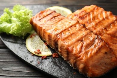 Photo of Delicious grilled salmon fillets with lettuce and lemon on wooden table, closeup