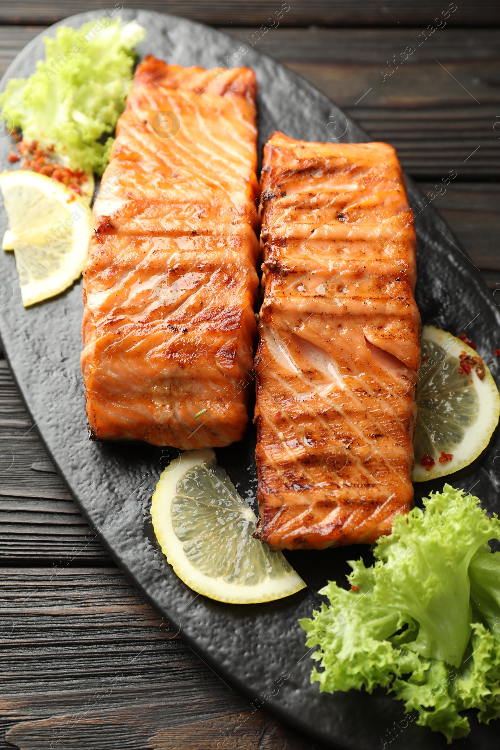 Photo of Delicious grilled salmon fillets with lettuce and lemon on wooden table, closeup