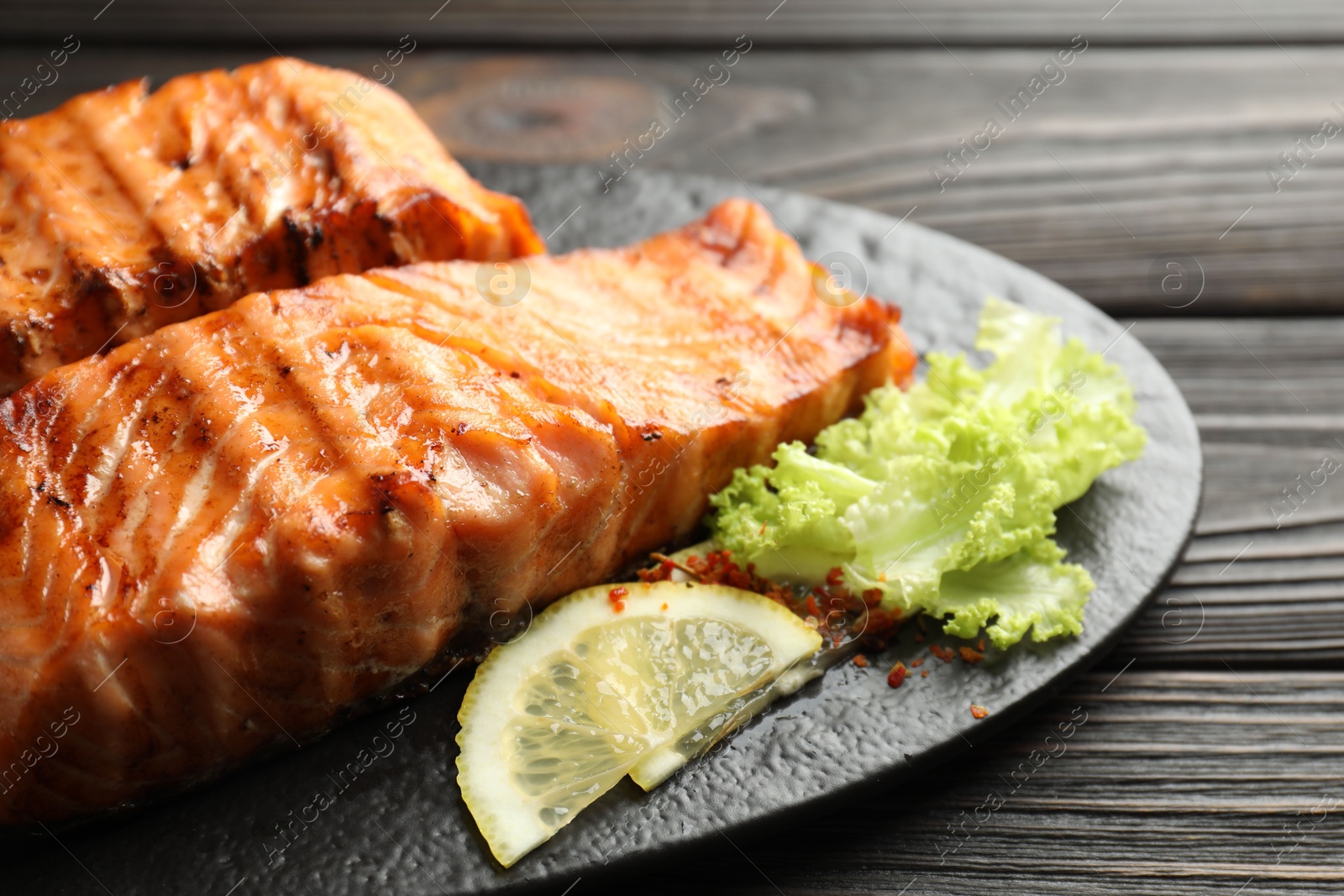 Photo of Delicious grilled salmon fillets with lettuce and lemon on wooden table, closeup