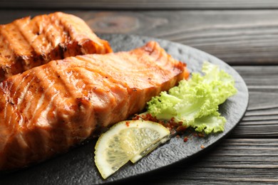 Photo of Delicious grilled salmon fillets with lettuce and lemon on wooden table, closeup