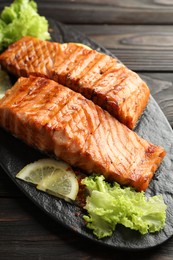 Delicious grilled salmon fillets with lettuce and lemon on wooden table, closeup