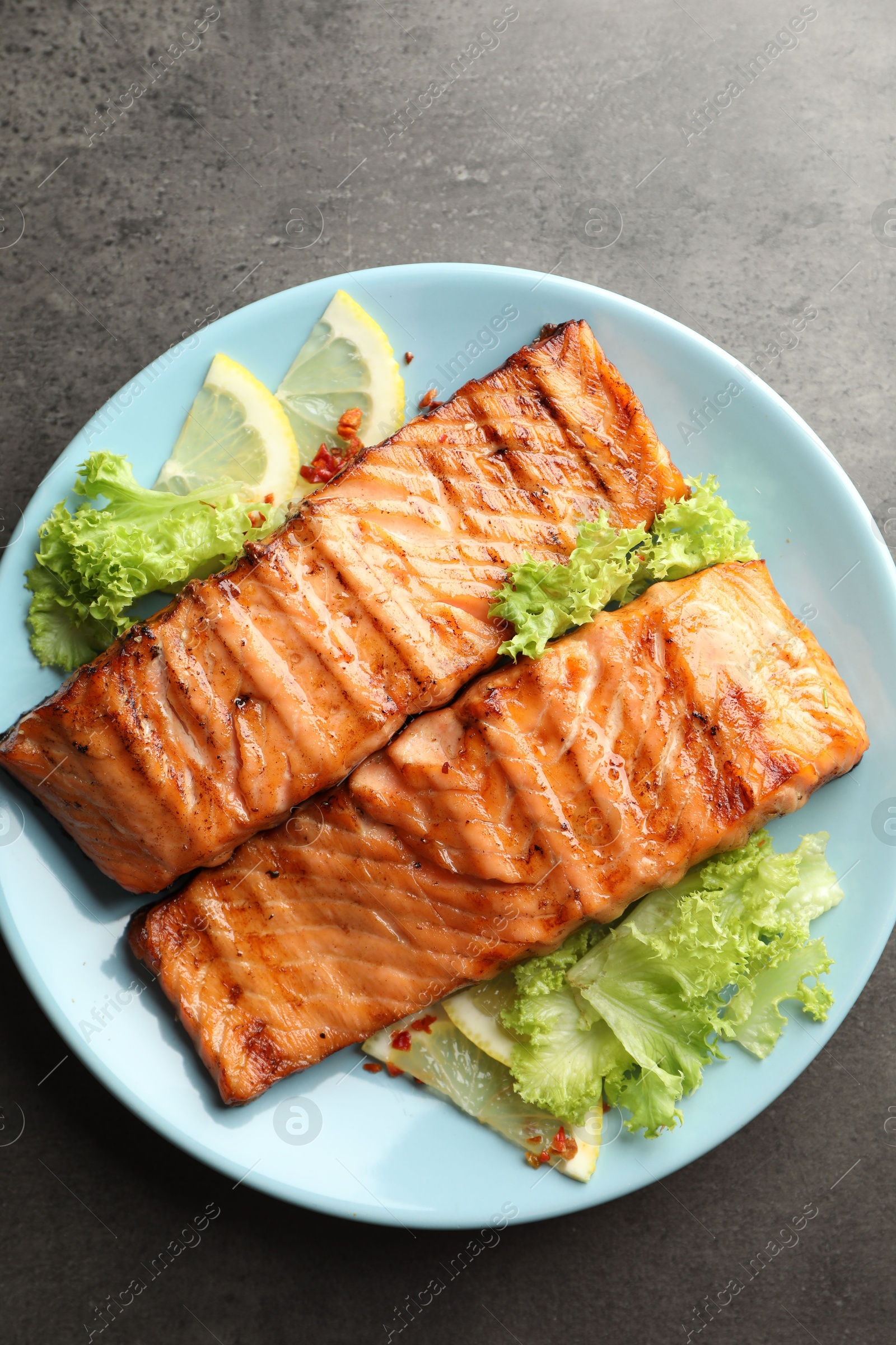 Photo of Delicious grilled salmon fillets with lettuce and lemon on grey table, top view