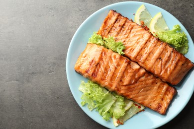 Photo of Delicious grilled salmon fillets with lettuce and lemon on grey table, top view. Space for text