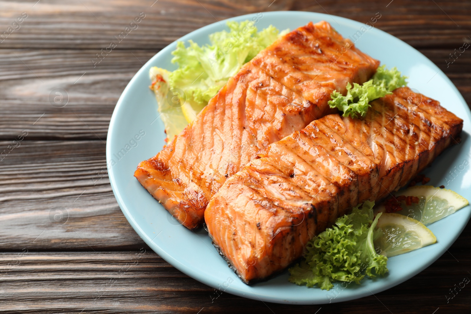 Photo of Delicious grilled salmon fillets with lettuce and lemon on wooden table, closeup