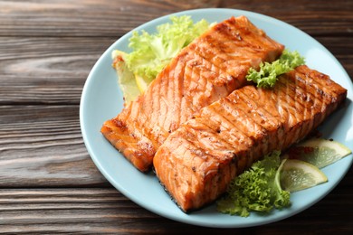 Photo of Delicious grilled salmon fillets with lettuce and lemon on wooden table, closeup