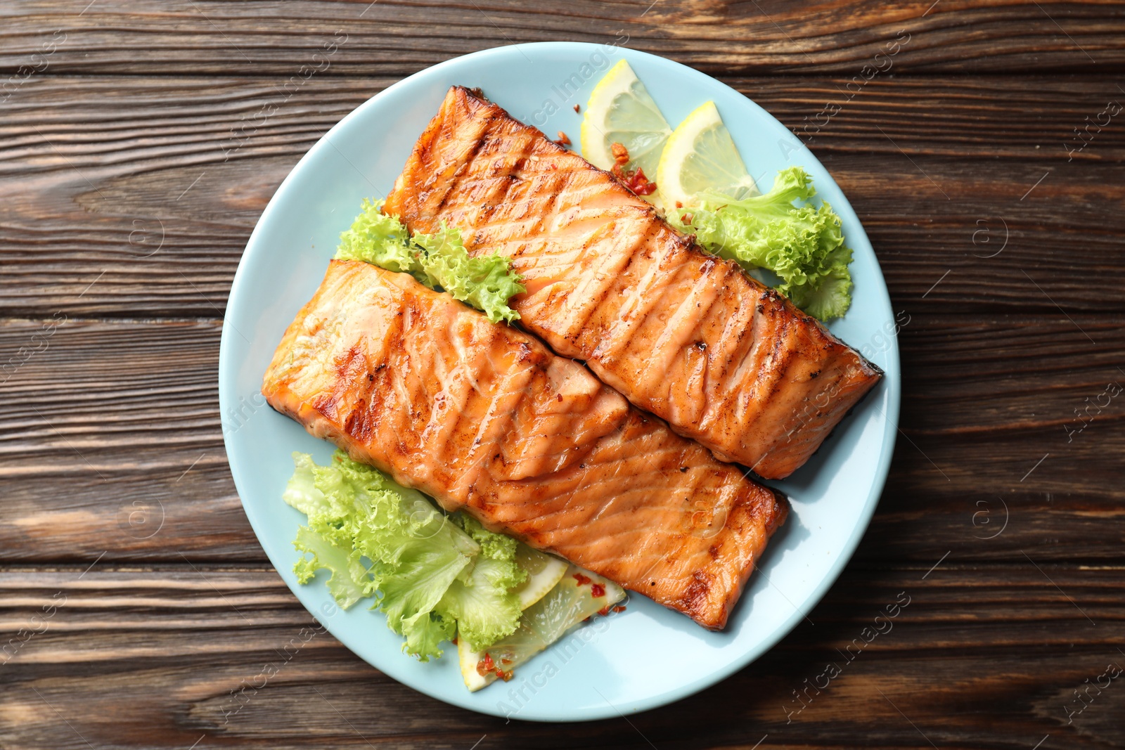 Photo of Delicious grilled salmon fillets with lettuce and lemon on wooden table, top view