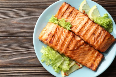 Delicious grilled salmon fillets with lettuce and lemon on wooden table, top view