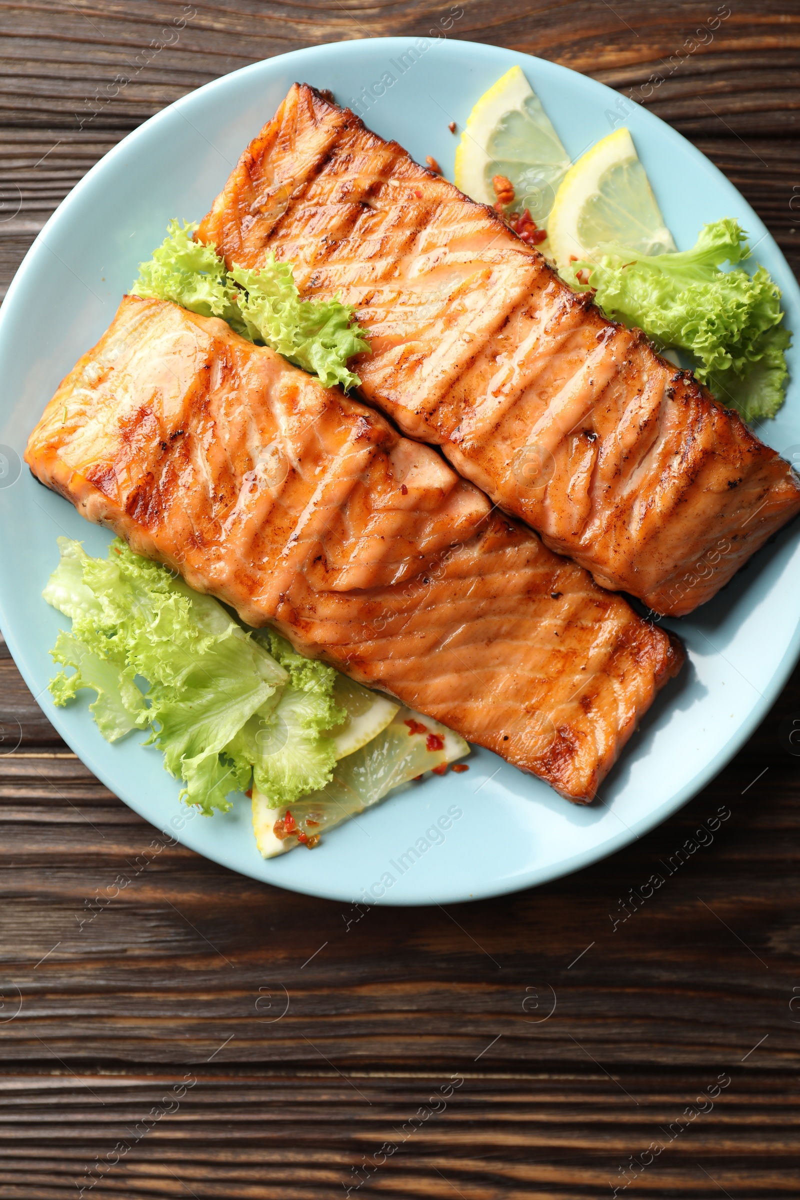 Photo of Delicious grilled salmon fillets with lettuce and lemon on wooden table, top view