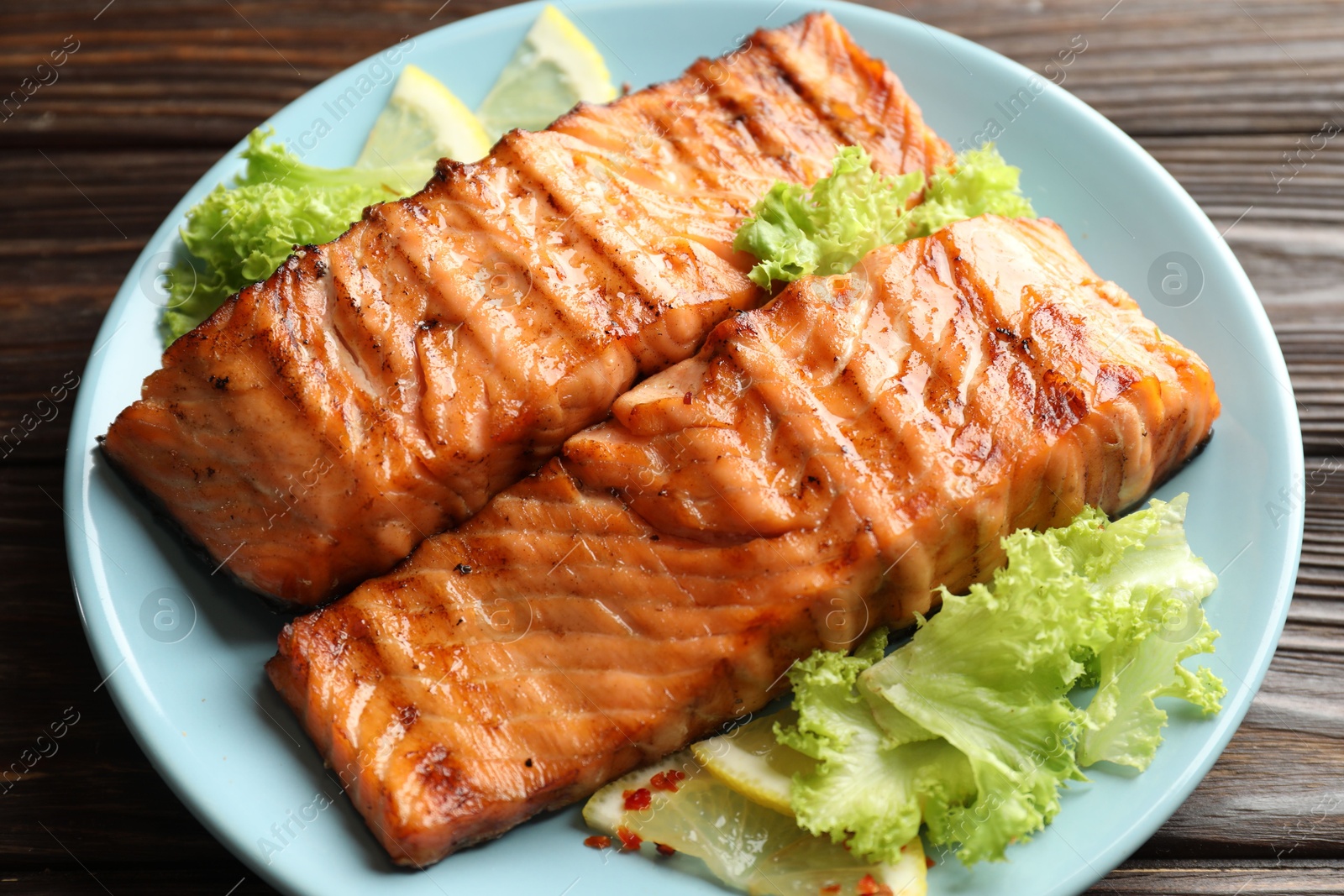 Photo of Delicious grilled salmon fillets with lettuce and lemon on wooden table, closeup