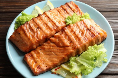 Photo of Delicious grilled salmon fillets with lettuce and lemon on wooden table, closeup