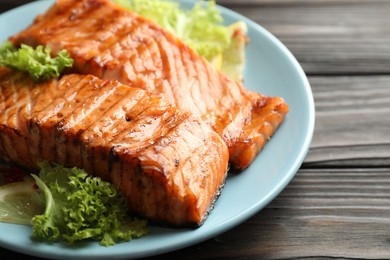 Delicious grilled salmon fillets with lettuce and lemon on wooden table, closeup