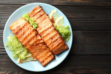 Photo of Delicious grilled salmon fillets with lettuce and lemon on wooden table, top view. Space for text