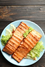 Photo of Delicious grilled salmon fillets with lettuce and lemon on wooden table, top view