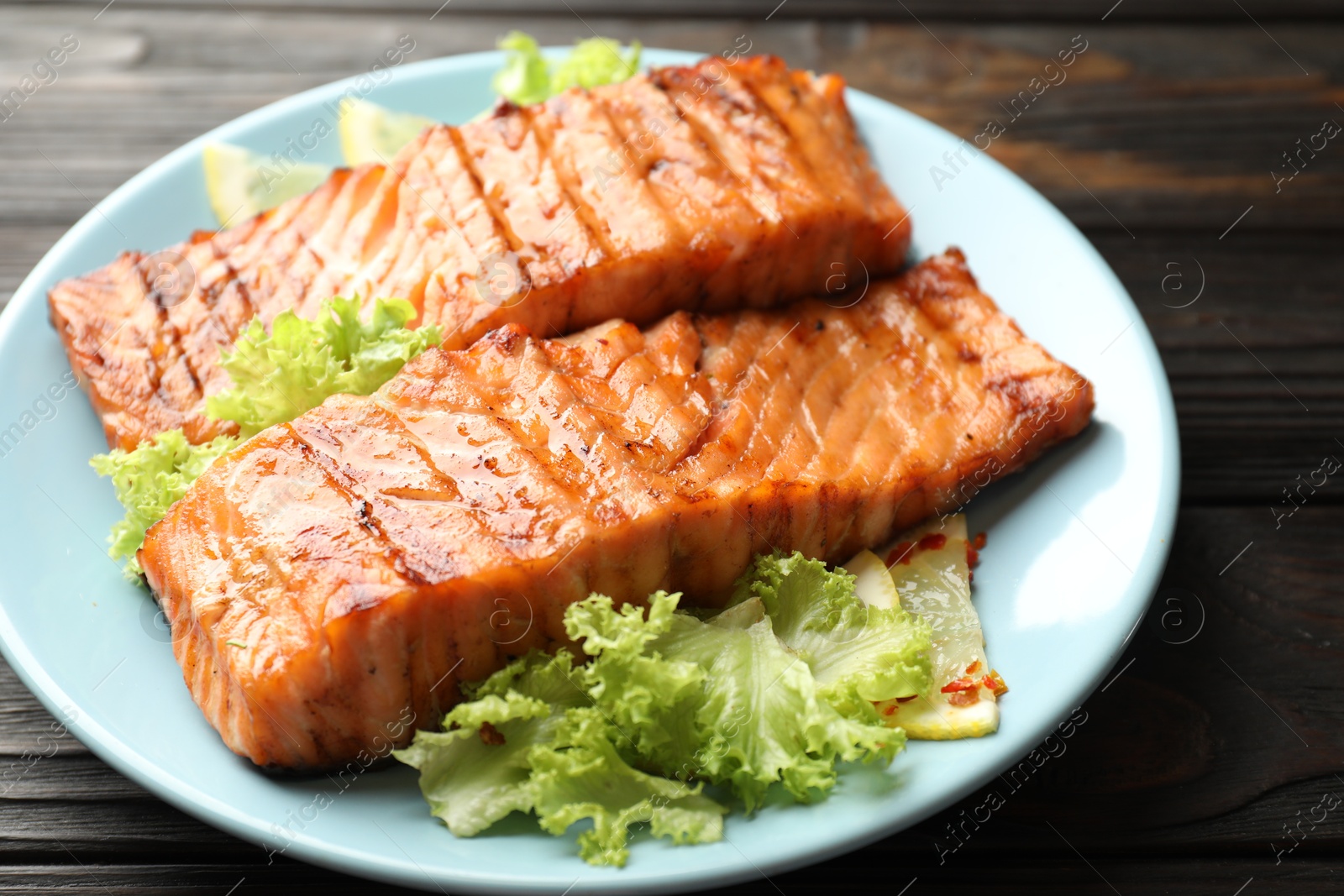 Photo of Delicious grilled salmon fillets with lettuce and lemon on wooden table, closeup