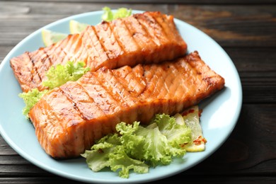 Photo of Delicious grilled salmon fillets with lettuce and lemon on wooden table, closeup