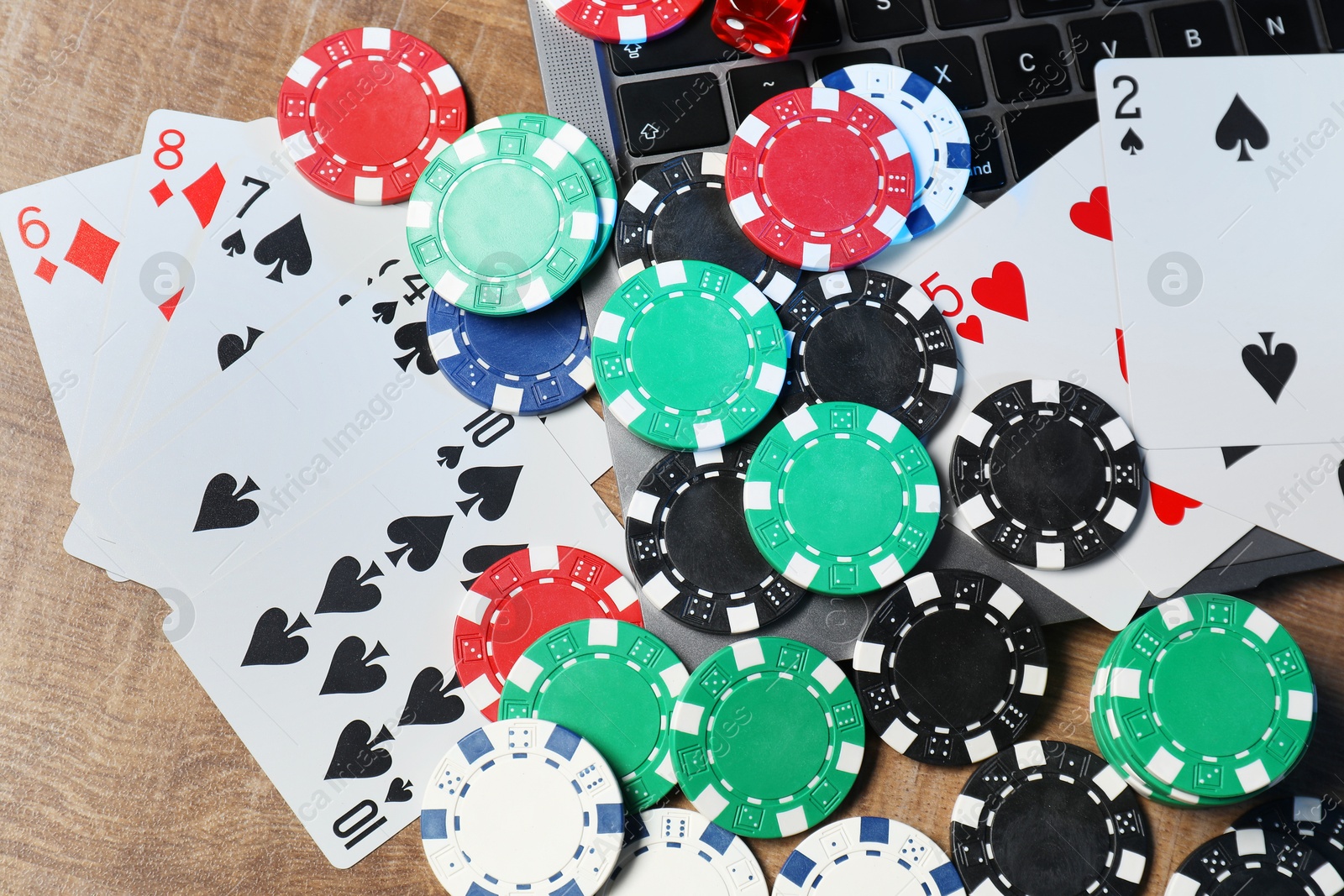 Photo of Poker chips, laptop, playing cards and dice on wooden table, flat lay. Online game