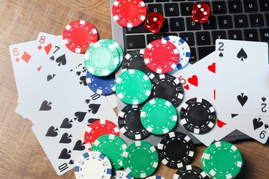 Poker chips, laptop, playing cards and dices on wooden table, flat lay. Online game