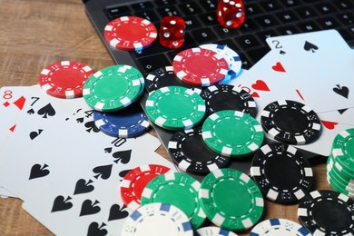 Poker chips, laptop, playing cards and dices on wooden table, closeup. Online game