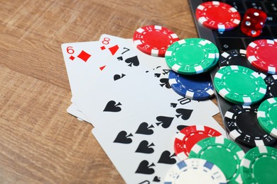 Photo of Poker chips, laptop, playing cards and dice on wooden table, closeup. Online game