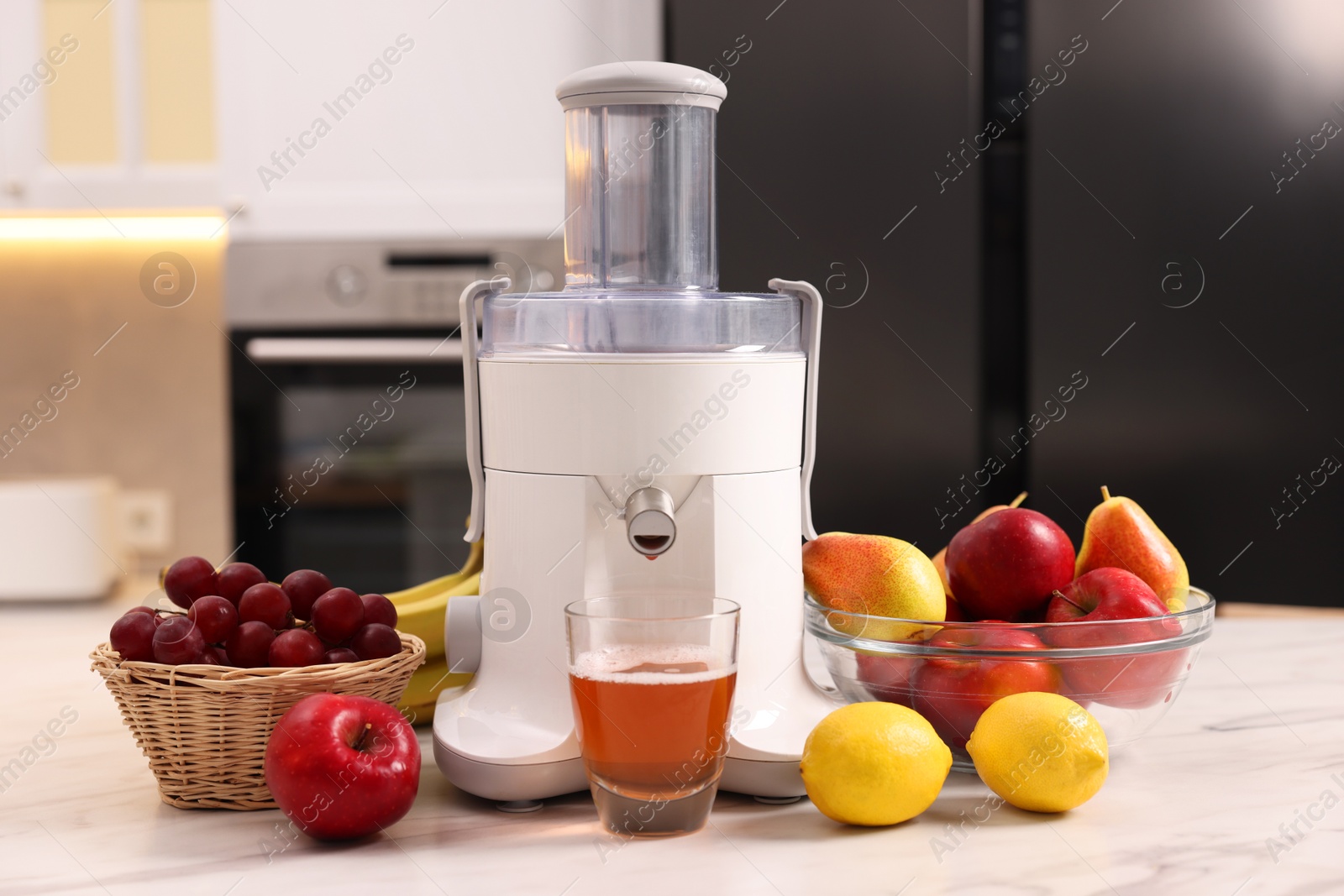 Photo of Modern juicer, fresh fruits and glass on white marble table in kitchen