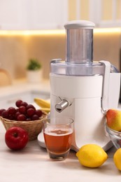 Photo of Modern juicer, fresh fruits and glass on white marble table in kitchen