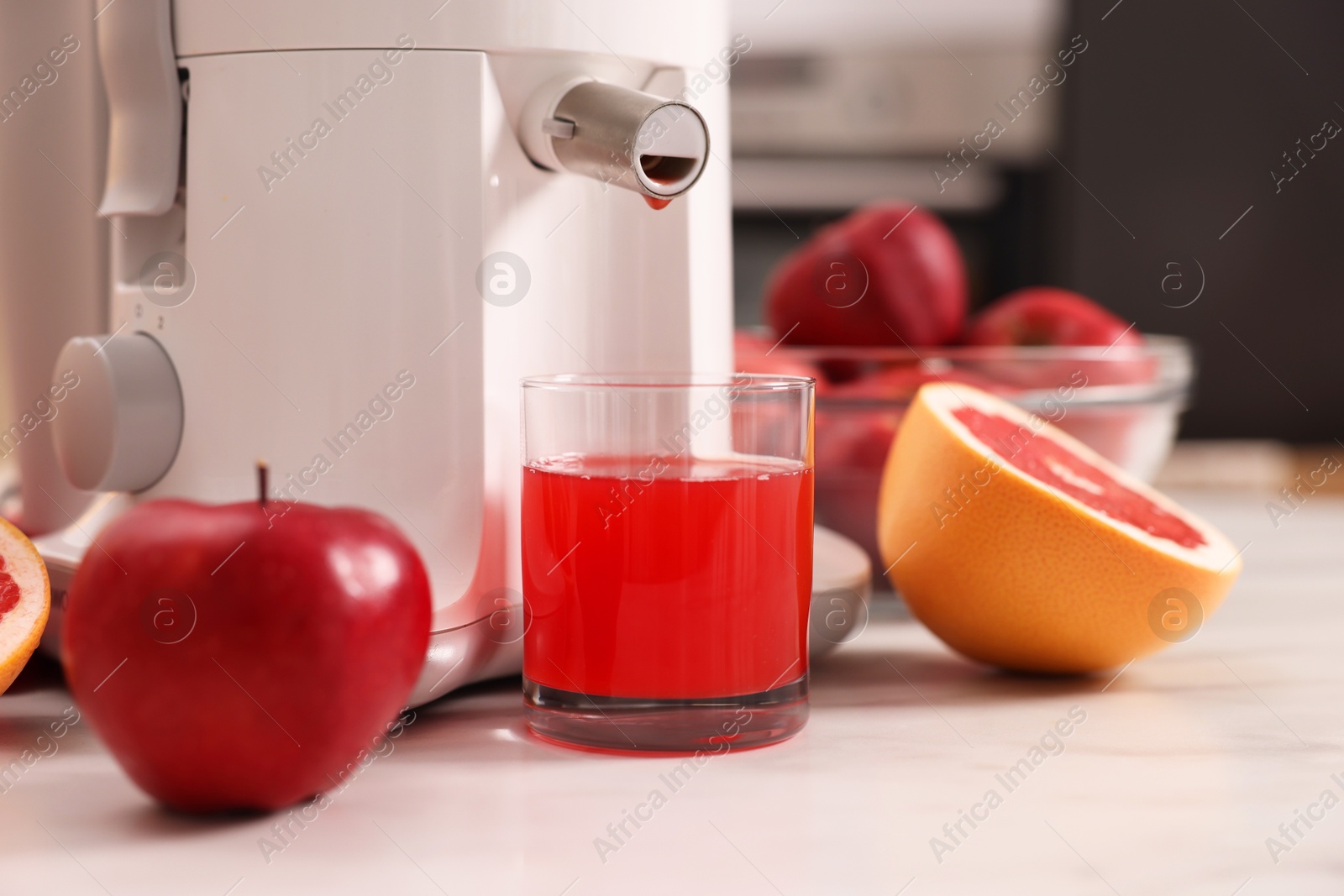 Photo of Modern juicer, fresh fruits and glass on white marble table in kitchen, closeup