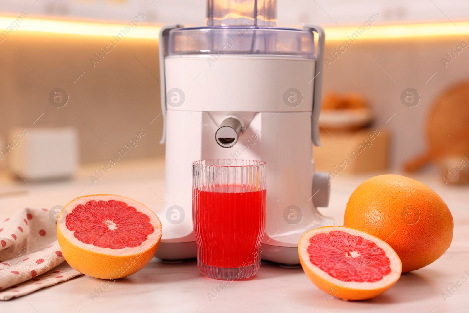 Photo of Modern juicer, fresh grapefruits and glass on white marble table in kitchen