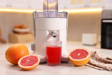 Photo of Modern juicer, fresh grapefruits and glass on white marble table in kitchen