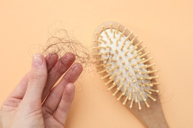 Photo of Woman taking her lost hair from brush on beige background, top view