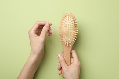 Photo of Woman taking her lost hair from brush on light olive background, top view. Alopecia problem