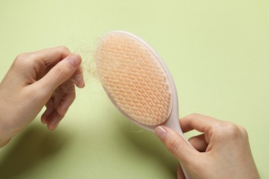 Photo of Woman taking her lost hair from brush on light olive background, closeup. Alopecia problem