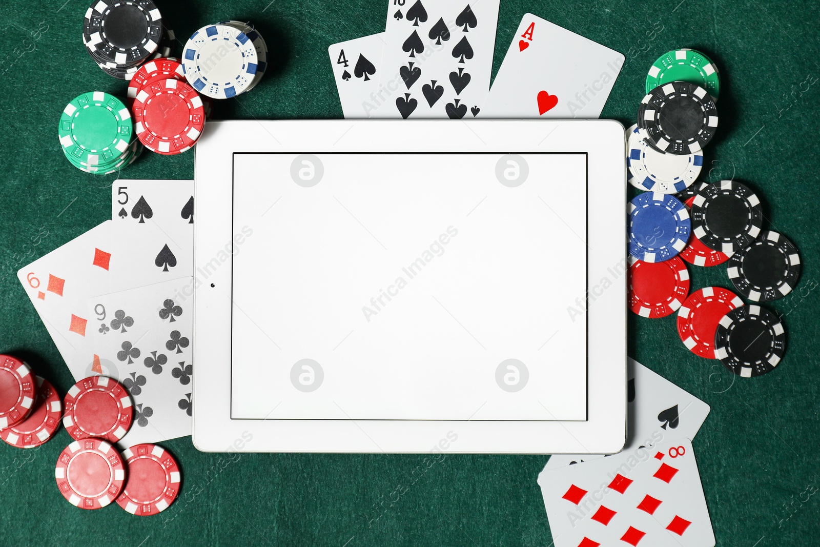 Photo of Poker chips, tablet and playing cards on green table, flat lay. Online game