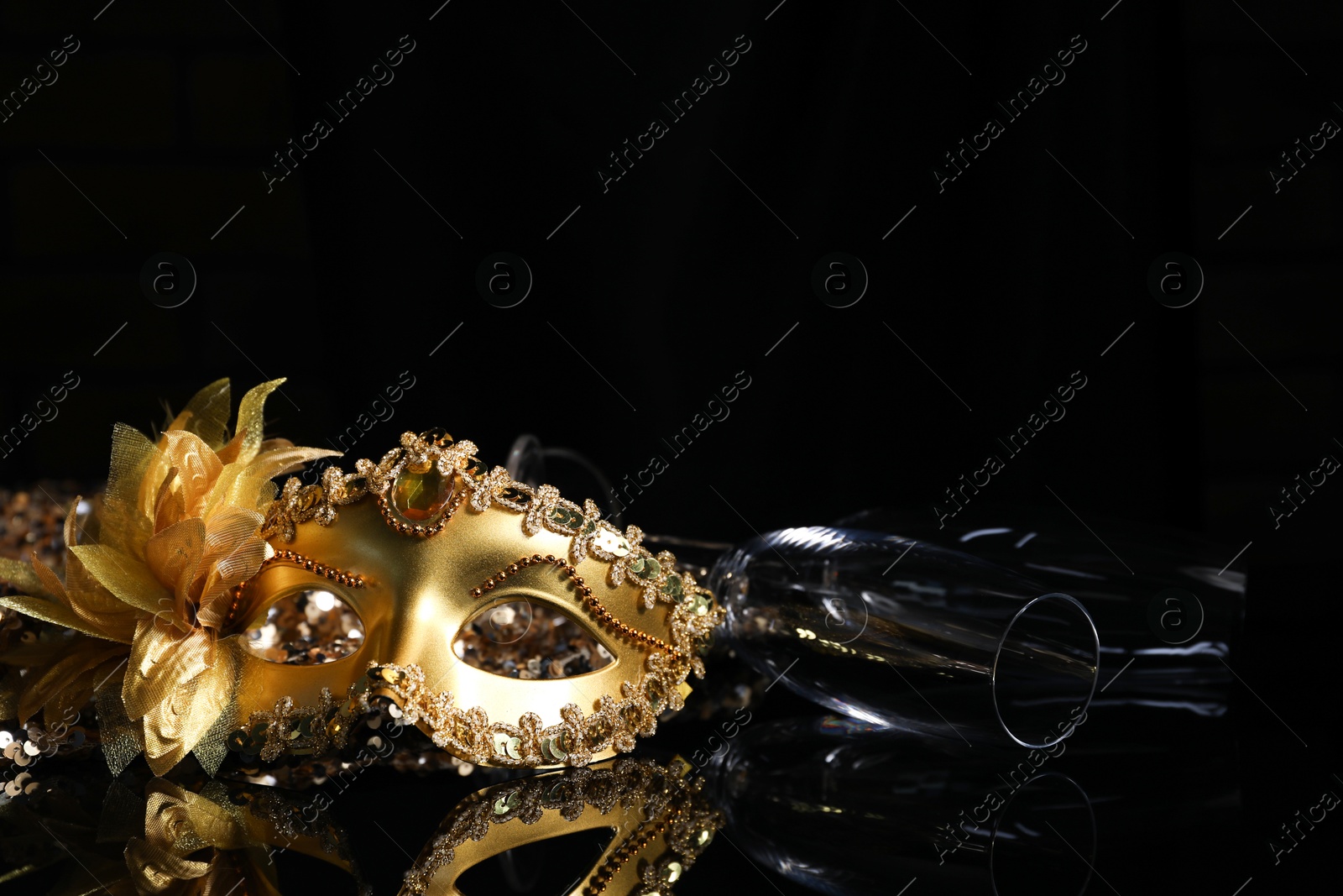 Photo of Beautiful golden carnival mask and champagne glass on black background, closeup. Space for text