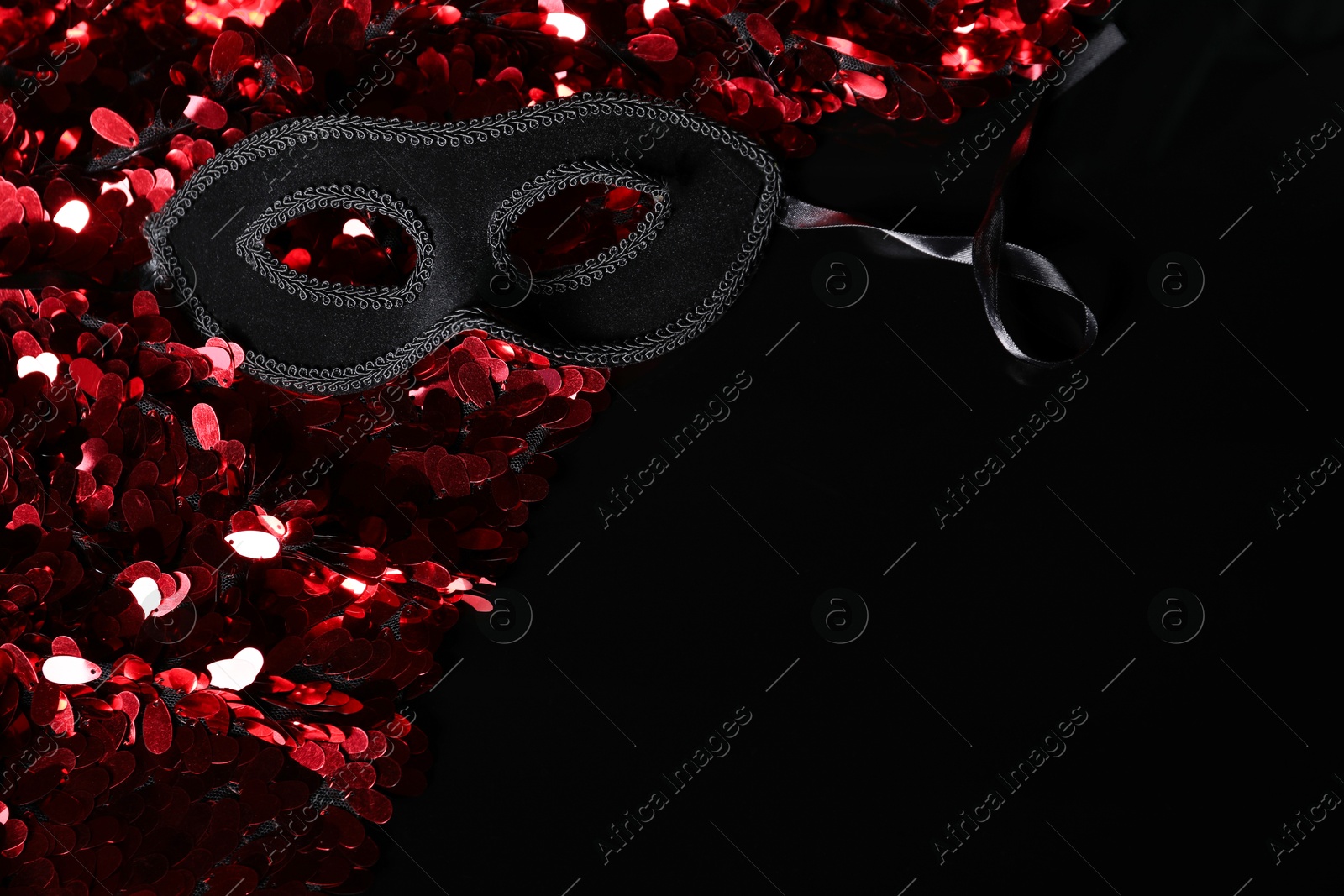 Photo of Beautiful golden carnival masks and fabric with red sequins on black background, closeup. Space for text