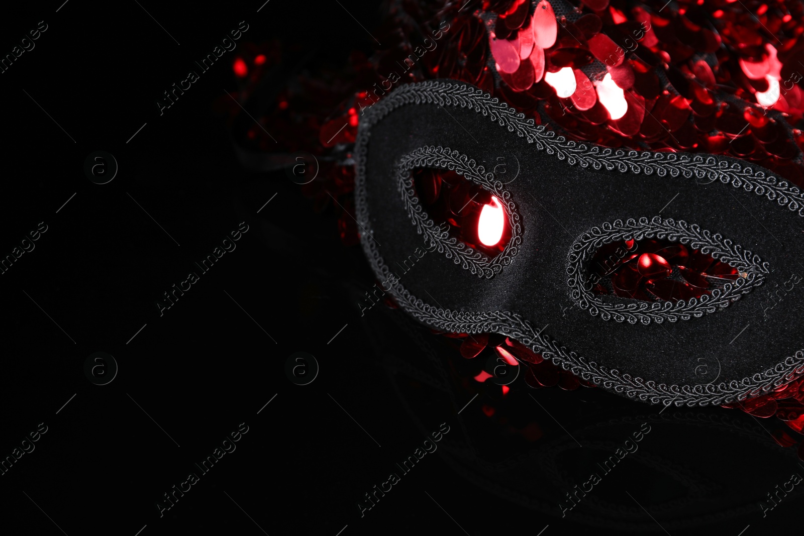 Photo of Beautiful golden carnival masks and fabric with red sequins on black background, closeup. Space for text