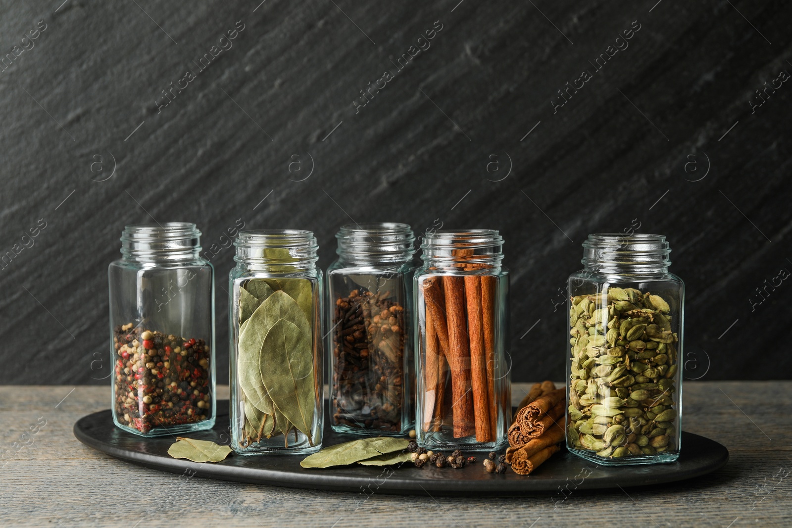 Photo of Different spices in glass jars on grey wooden table, closeup